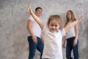 A young girl smiling brightly with her arms outstretched in a joyful pose, representing the confidence and freedom a child feels when they successfully adapt to a new country.