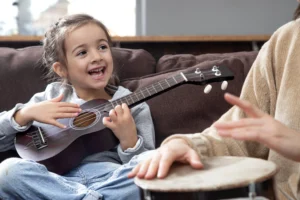 A happy child laughing while playing a ukulele and a drum in a playful music-based language learning class.