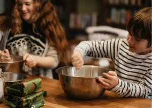 Two children focused on mixing ingredients in metal bowls during a shared baking project at a supportive kids' camp.