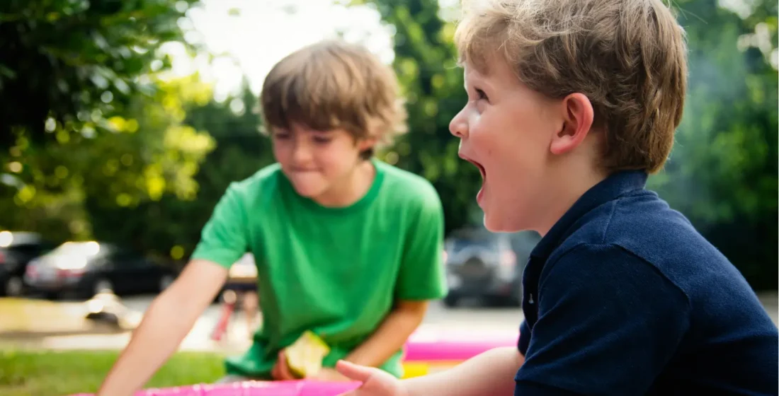A joyful young boy laughing while playing in a colorful outdoor setting with a friend, illustrating a gentle entry point for settling in a new country.