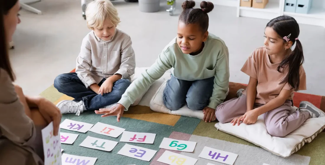 Three young children sitting on a colorful rug in a classroom, happily engaging with alphabet cards during a group learning activity.
