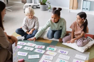 Three young children sitting on a colorful rug in a classroom, happily engaging with alphabet cards during a group learning activity.