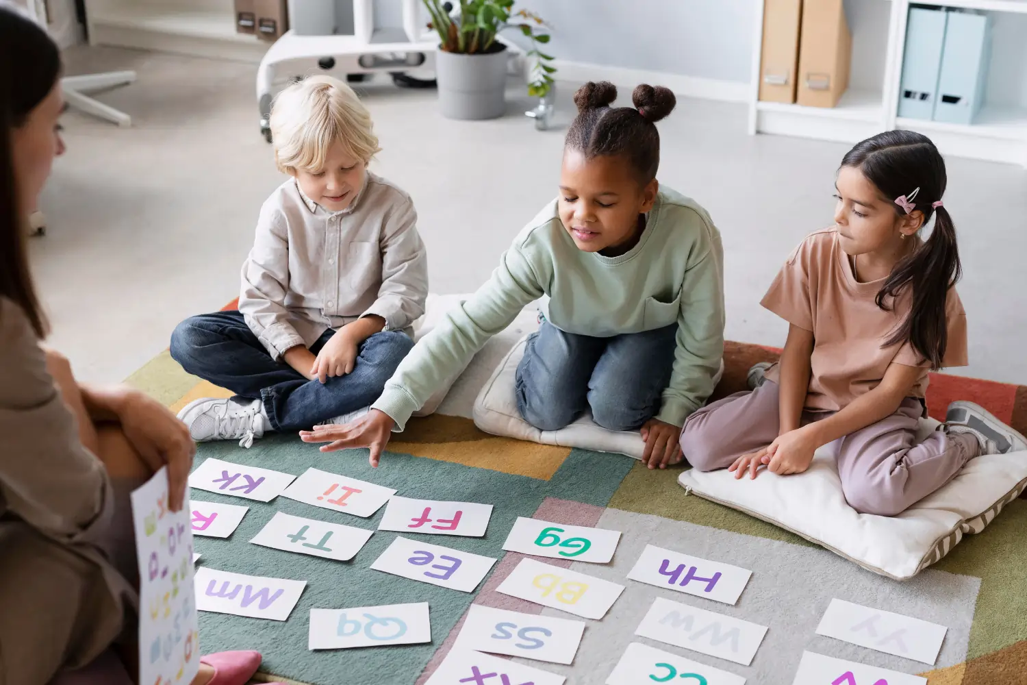 Three young children sitting on a colorful rug in a classroom, happily engaging with alphabet cards during a group learning activity.