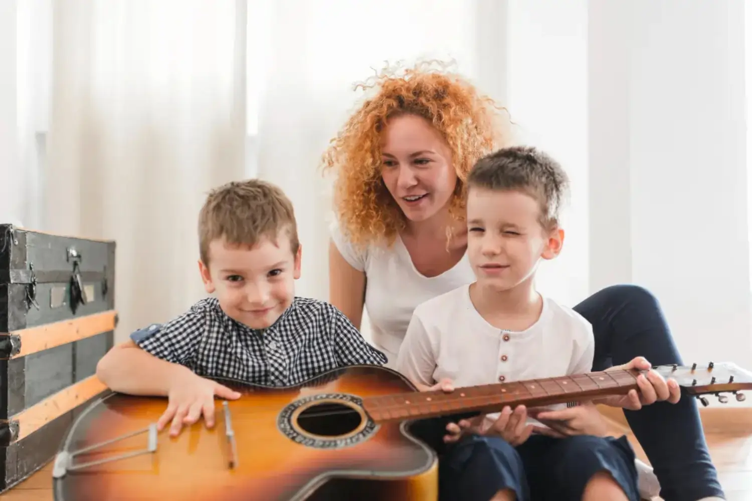 Two young children sitting on a wooden floor playing together with a guitar in a low-pressure learning environment.