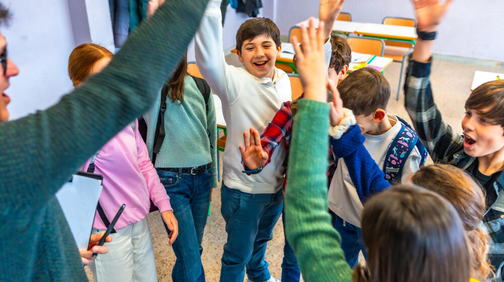 A group of happy young students in a classroom giving energetic high-fives to their teacher.