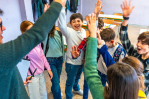A group of happy young students in a classroom giving energetic high-fives to their teacher.